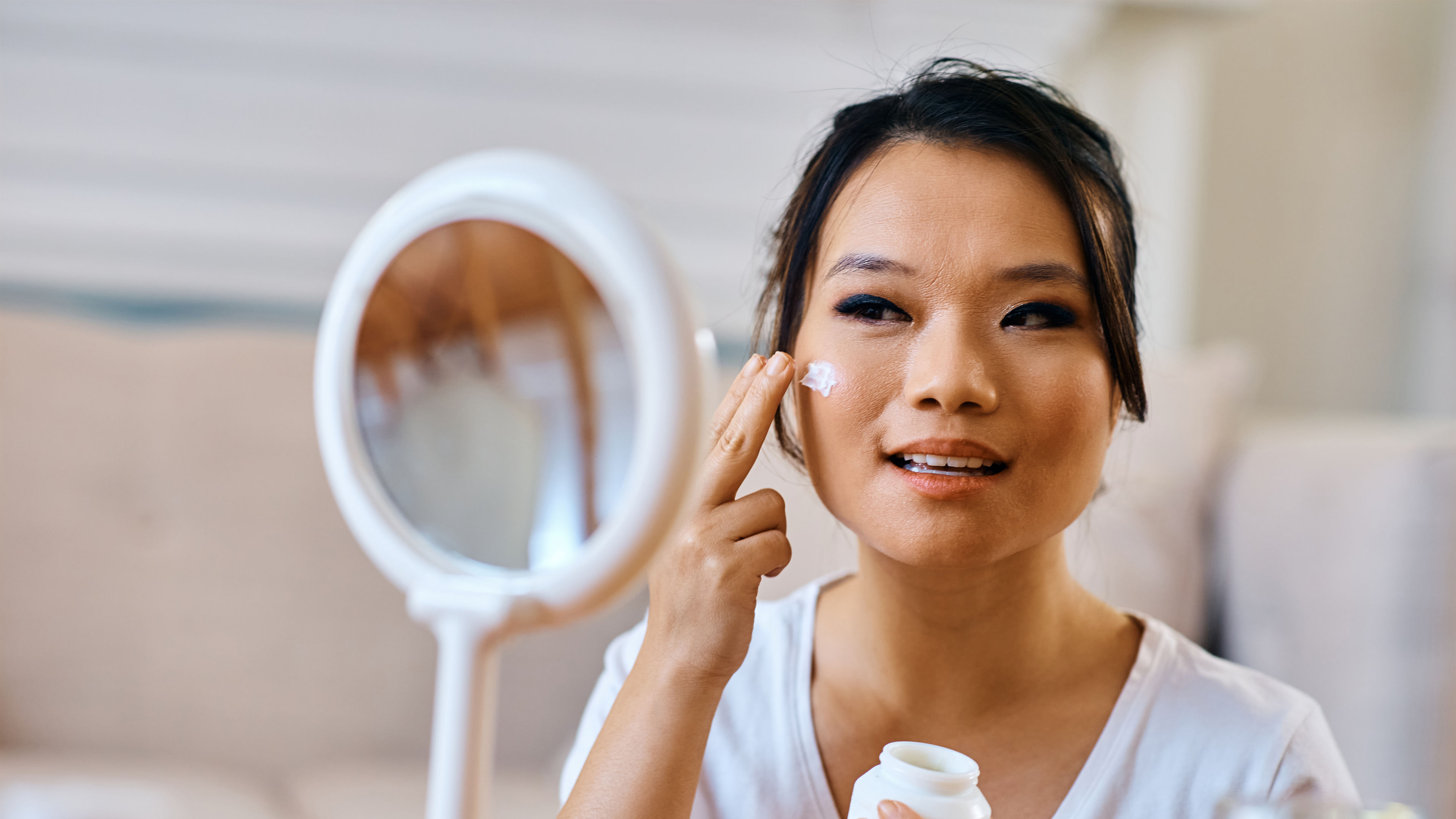 Young Asian woman applying moisturizer on her face skin.