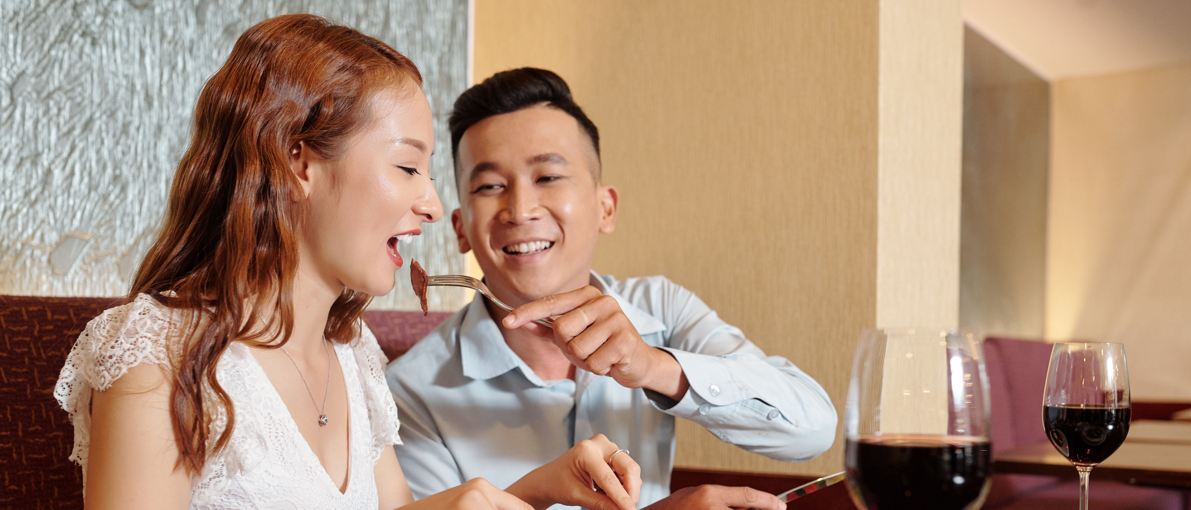 Happy smiling young man feeding girlfriend with piece of meat